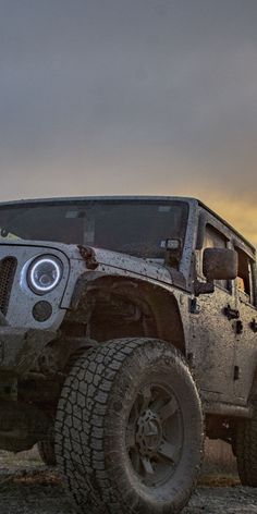 a jeep parked in the middle of an open field at sunset with its lights on