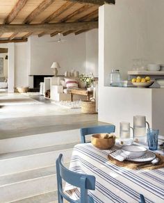 a dining table with blue chairs and plates on it in front of an open kitchen