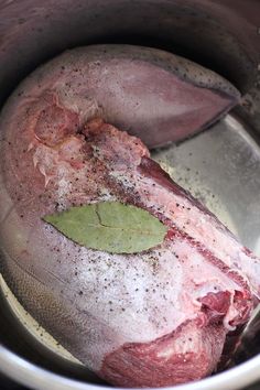 a raw meat in a pot with a leaf on the side and seasoning sprinkles