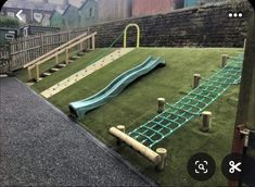 an artificial play area with a slide and climbing bars in the grass, next to a brick wall