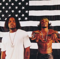 two men standing next to each other in front of an american flag with chains on their arms