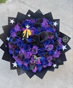 a bouquet of purple and black flowers with a yellow stuffed animal on top is sitting on the ground