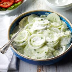 a blue bowl filled with cucumber salad next to bowls of tomatoes and lettuce