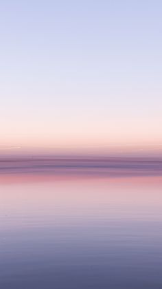 the sky is pink and purple as it reflects in the calm water on an empty beach