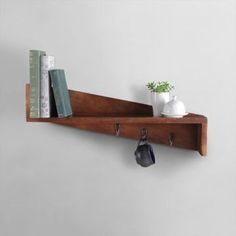 a wooden shelf with two hooks holding books and a coffee cup on the wall next to a potted plant