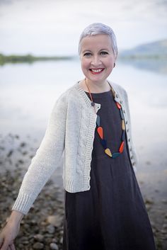 a woman with white hair is standing by the water wearing a sweater and colorful necklace