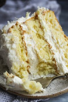 a piece of white cake on a plate with a fork in the foreground and a napkin behind it