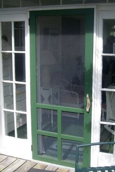 a green door on the side of a house with glass panes and an iron bench