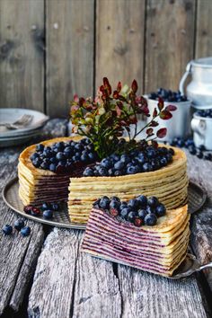 a layered cake with blueberries and berries on top is sitting on a wooden table