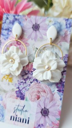 white flower earrings with gold hoops on top of a greeting card next to flowers