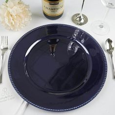 there is a blue plate and silverware on the table next to a bottle of wine