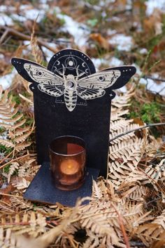 a candle holder sitting on top of dry grass with a glass in front of it