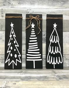 three black and white christmas trees are hanging on wood planks, tied with twine