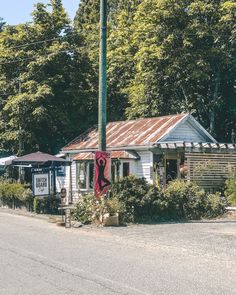 a small white building sitting on the side of a road next to a lush green forest