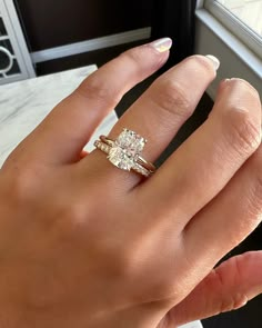 a woman's hand with a diamond ring on top of her finger, next to a window