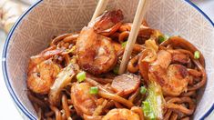 a bowl filled with stir fry noodles and shrimp, topped with chopsticks in it