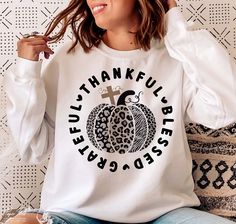 a woman sitting on a couch wearing a white sweatshirt with leopard print pumpkin and cross