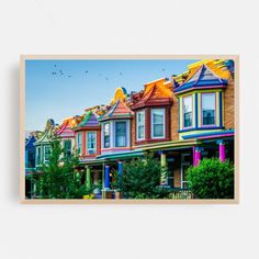 a row of colorful houses with birds flying in the sky above them and on top of one another