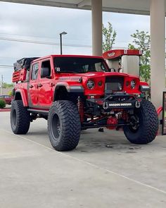 a red jeep is parked in front of a gas station with two large tires on it