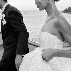 the bride and groom are walking together by the water on their wedding day in black and white