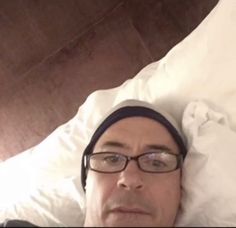 a man laying in bed with his head on the pillow and looking at the camera