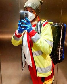 a woman in yellow jacket and blue gloves taking a selfie with her cell phone