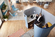 two people sitting at a desk in an office cubicle with chairs and rugs on the floor