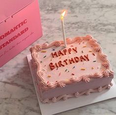 a birthday cake sitting on top of a table next to a pink box with a lit candle