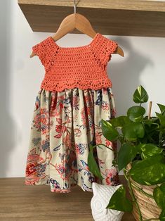 a dress hanging on a clothes rack next to a potted plant and wooden shelf