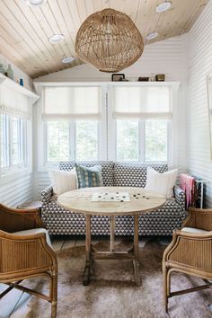 a living room with couches, chairs and a round table in front of two windows