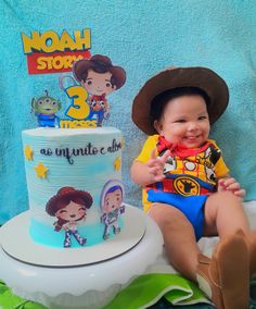 a baby sitting next to a cake with toy characters on it and a blue towel