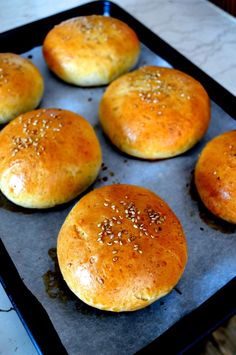 six rolls sitting on top of a baking pan covered in sesame seed sprinkles