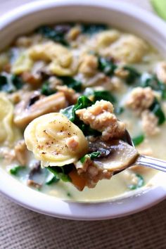 a white bowl filled with pasta and spinach covered in meat, cheese and broccoli