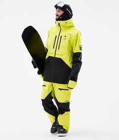 a man holding a snowboard while standing in front of a white background and wearing a yellow ski suit