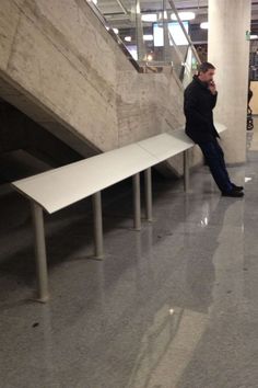 a man sitting on a bench talking on his cell phone in an empty building next to stairs