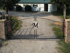 an iron gate with the letter m on it is in front of a large house