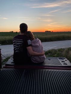 a man and woman sitting on the back of a pickup truck with their arms around each other