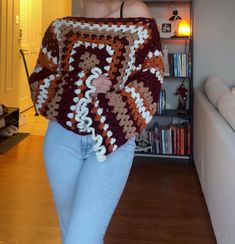 a woman is walking in the living room wearing a crocheted sweater and jeans