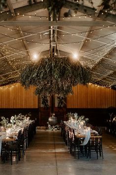 the tables are set up for an event with greenery hanging from the ceiling and fairy lights strung over them