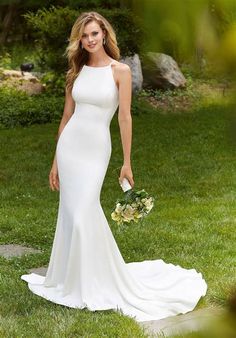 a woman in a white wedding dress standing on the grass holding a bouquet and looking at the camera