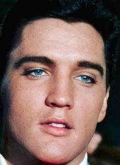 a close up of a person wearing a suit and tie with blue eyes looking at the camera