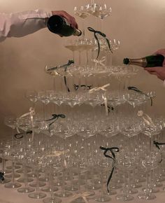 two people pouring champagne into wine glasses on top of a table filled with empty wine glasses