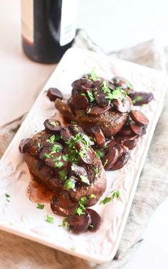 two pieces of meat covered in mushrooms and garnished with parsley on a white plate