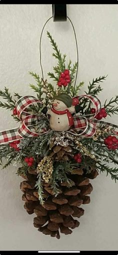 a pine cone ornament hanging on the wall with red berries and evergreen cones