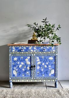 a blue and white cabinet with flowers painted on the doors, next to a potted plant