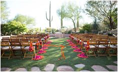 rows of wooden chairs with orange sashes and pink flowers on them in the grass