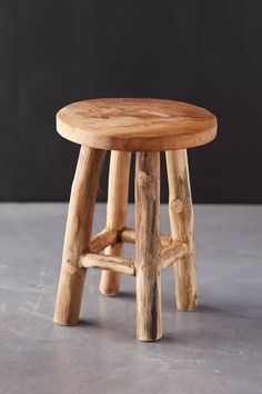 a wooden stool made out of logs sitting on top of a cement floor next to a black wall