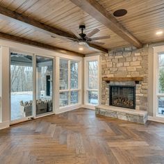 an empty living room with wood floors and stone fireplace in the center, surrounded by large windows