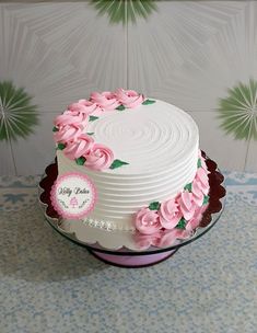 a white cake with pink flowers on it sitting on a table next to a wall