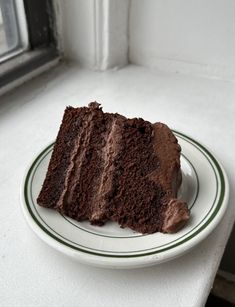 a piece of chocolate cake sitting on top of a white plate next to a window